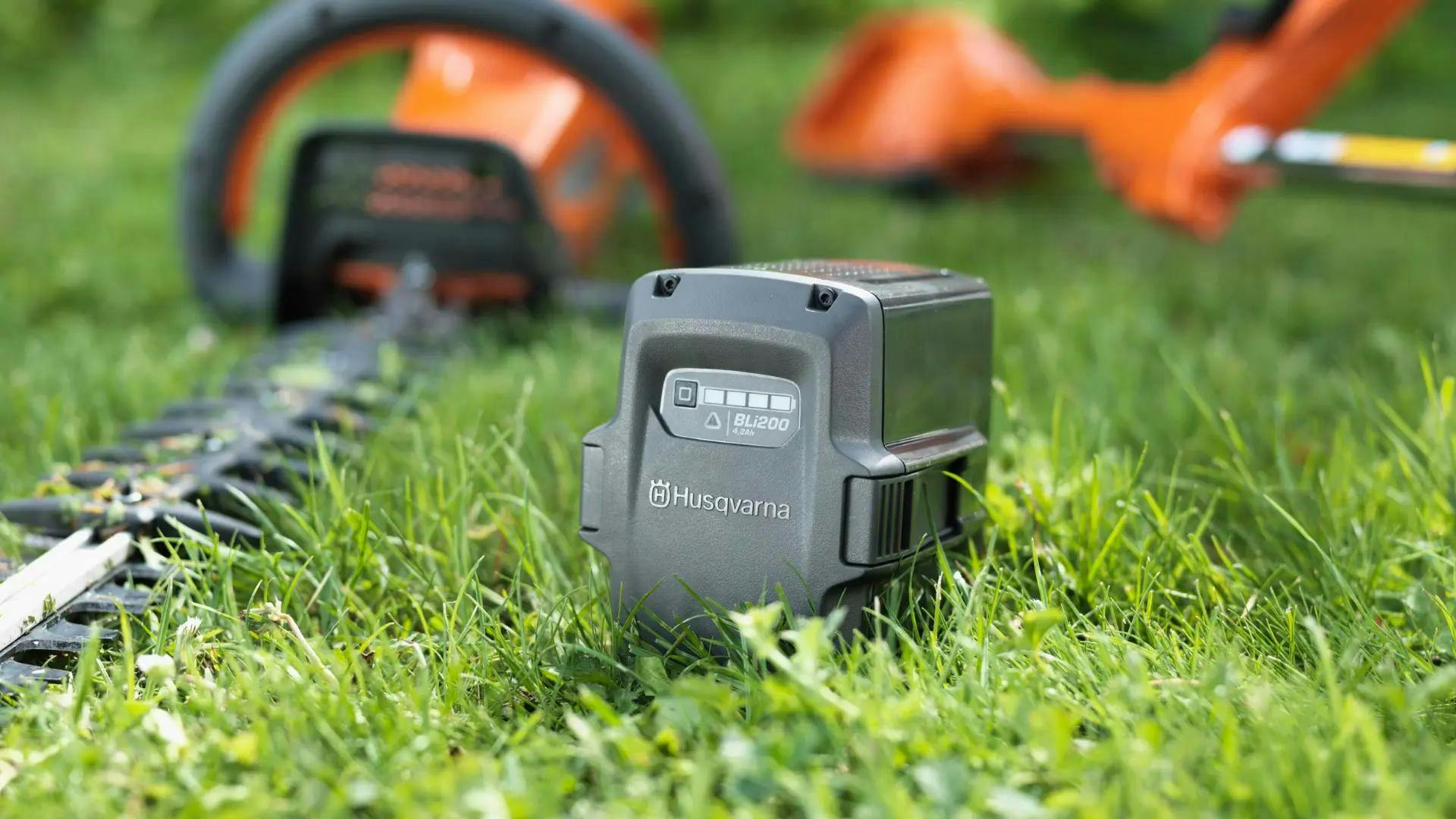 husqvarna battery sitting in grass with tools sitting behind